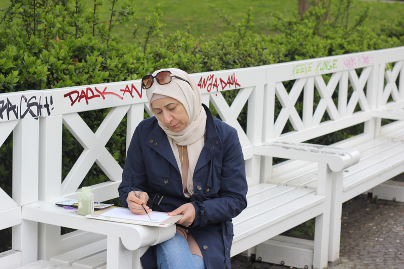 Wafaa sitzt auf einer Parkbank und malt